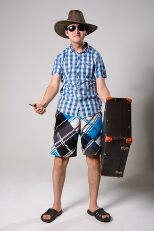 Portrait of young man in sunglasses with a suitcase in hand. Man in a hat with a phone in his hand.の写真素材
