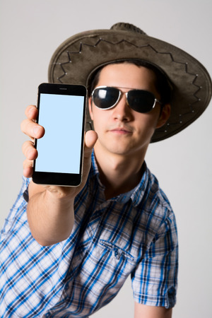 Young man wearing sunglasses and a hat in his hand phone shows.の写真素材