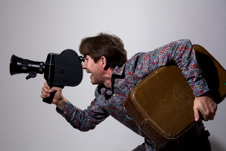 Portrait of a cameraman with old movie camera. Happy traveler with a suitcase on shooting video