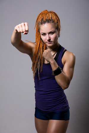 Young woman with dreadlocks in fighting stance on a gray backgroundの写真素材