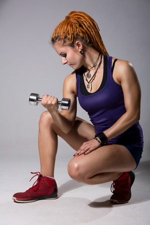 A young girl with dreadlocks training with dumbbells. Athlete fitnessa.na gray background in studioの写真素材
