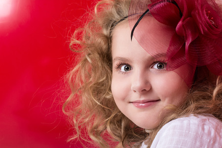 Close-up portrait of a beautiful girl in a red divlennoy hat. On a red backgroundの写真素材