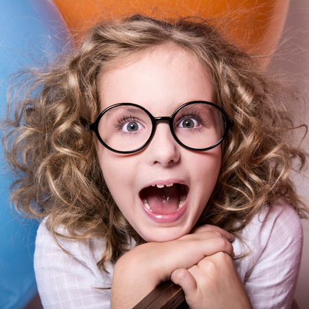 Happy surprised girl in glasses with an open mouth on a background of large balloons. square photoの写真素材