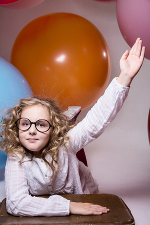 Girl in glasses with hand raised wants to ask. Against the background of the big balloonsの写真素材