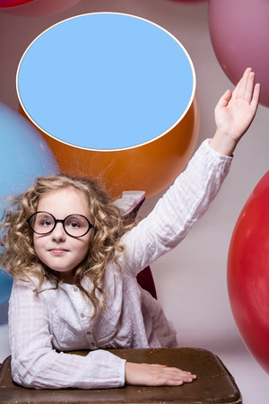 Girl in glasses with hand raised wants to ask. Against the background of the big balloons. Place for an inscriptionの写真素材
