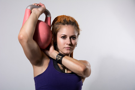 Portrait close up of young attractive female doing kettle bell exercise on grey background. Fitness woman working out. Crossfit exercise.の写真素材