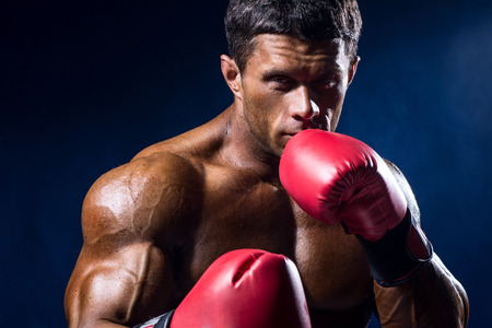 Close-up portrait of boxer in red boxing gloves on a dark blue background.