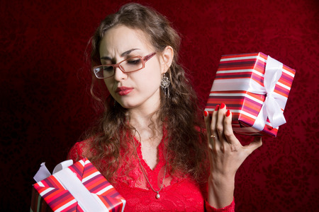 Thoughtful girl in glasses with two striped gift box. On a red backgroundの写真素材