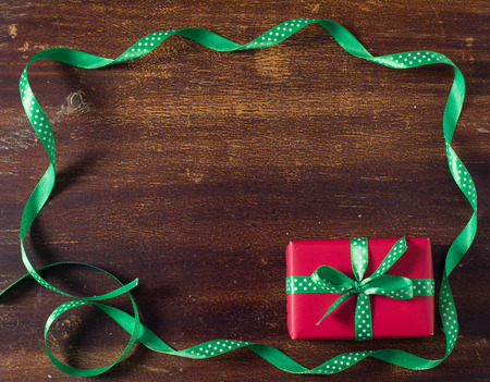 Red gift box with green ribbon lying on the wooden background.の写真素材