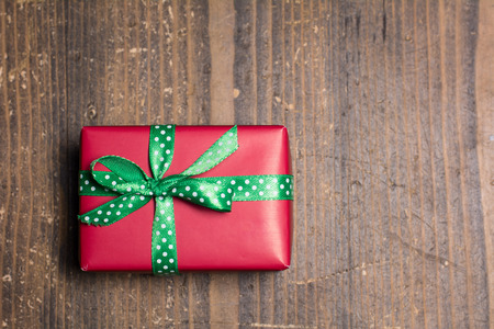 Red gift box with green ribbon with polka dots on a wood backgroundの写真素材