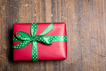 Red gift box with green ribbon with polka dots on a wood background.の写真素材