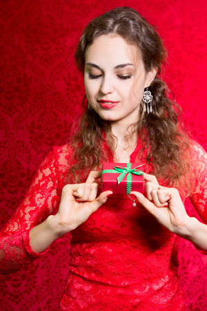 Beautiful curious girl with a small gift in a red dress. A gift for the new year, Christmas, birthday, Valentine's Dayの写真素材