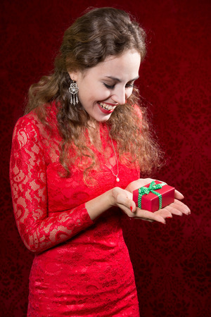 Happy young woman with a small gift in a red dress. A gift for the new year, Christmas, birthday, Valentine's Dayの写真素材