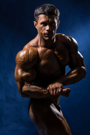 Handsome muscular bodybuilder posing over blue background.の写真素材