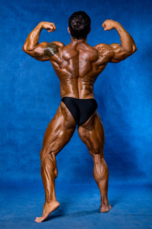 Athletic sports bodybuilder demonstrates posture from the back. Mandatory poses bodybuilders. On a blue backgroundの写真素材