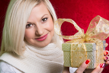 A girl in a white sweater with a gift bow with bandaged looking at the camera. Close-up portrait of a beautiful young woman on a red background. Holiday Saleの写真素材