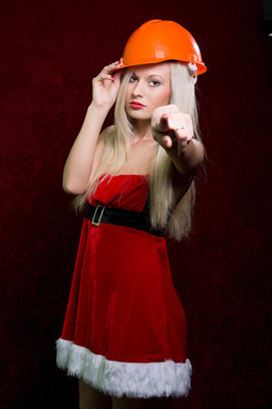 Portrait of a young girl in a Santa suit and helmet of the builder pointing his finger at the camera.の写真素材