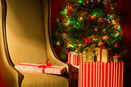 Christmas interior with illuminated Christmas tree and chair. Gifts at the Christmas tree. New Year's holiday. Horizontal image.の写真素材