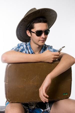 Portrait of young man in sunglasses with a suitcase. traveler in a hat with a phone in his hand.の写真素材
