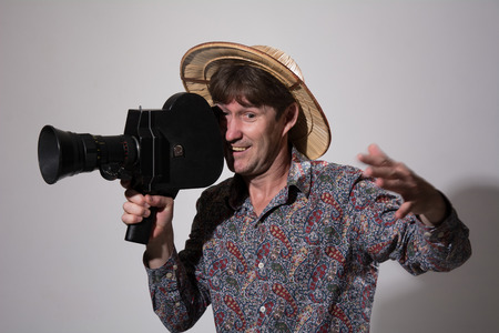 A man in a straw hat with an old movie camera on a gray background. Videographer to capture