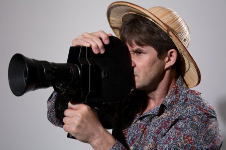A man in a straw hat with an old movie camera on a gray background. Videographer to shoot reportageの写真素材