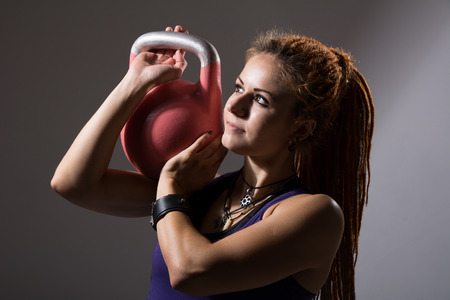 Portrait close up of young attractive female doing kettle bell exercise on grey background. Fitness woman working out. Crossfit exercise.の写真素材