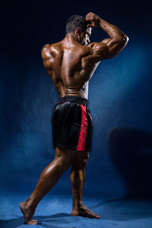 Portrait in full growth bodybuilder. Looking away and shows his biceps on a blue backgroundの写真素材