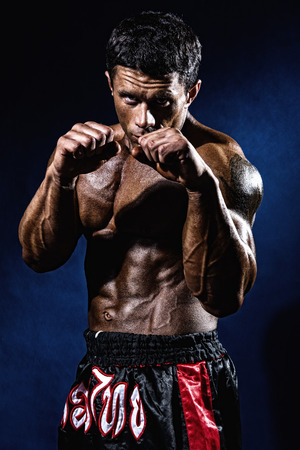 Fighter in a rack with fists on a blue background. Portrait of a kick-boxerの写真素材