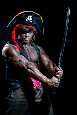 Muscular black man in a pirate hat and sword on a black background.の写真素材