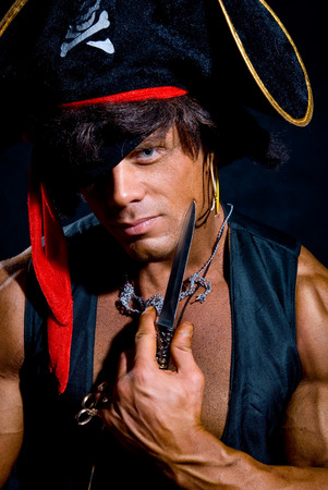 Close-up portrait muscular pirate with a knife on a dark background. A man looking at the cameraの写真素材