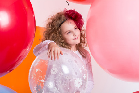 Young teen girl in a hat and white dress on a background of large air rubber balls. Cheerful girl looking to the sideの写真素材
