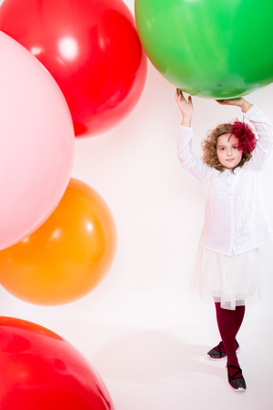 Teen girl in a hat and white dress on a background of big colored rubber air balls.の写真素材