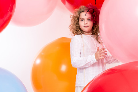 Teen girl in a hat and white dress on a background of big colored rubber air balls.の写真素材