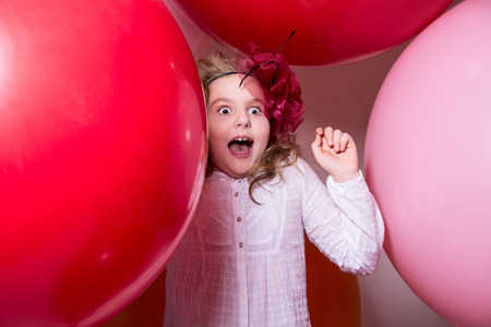 Surprised, the frightened teen girl in white dress and hat. Against the background of big colorful balloonsの写真素材