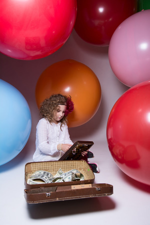 Beautiful teen girl with wooden abacus and a suitcase full of money on the background of large rubber balloonsの写真素材