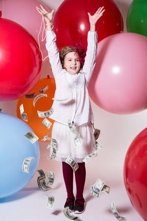 Happy teen girl and falling on top of dollars. Against the background of colored rubber ballsの写真素材