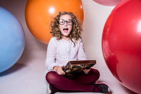 Screaming curly teen girl in glasses with wooden abacus on the background of large rubber balls.の写真素材