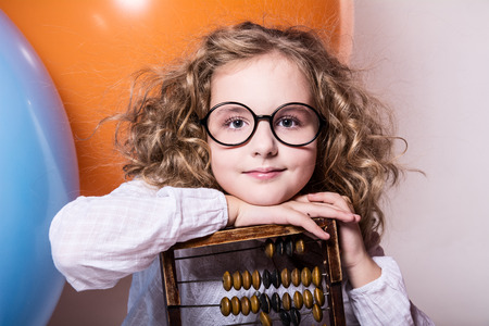 Funny, clever curly teen girl in glasses with wooden abacus on the background of large rubber balls.の写真素材
