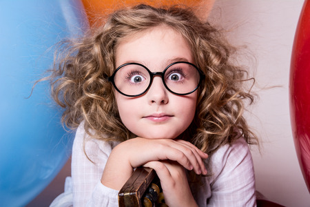 Portrait of surprised curly teen girl in glasses on the background of large rubber balls. Girl looking at the cameraの写真素材