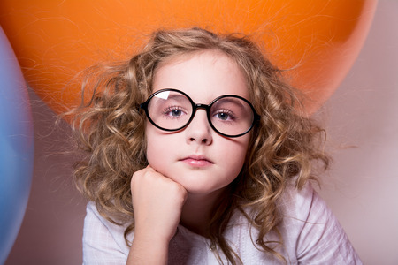 Beautiful, smart curly teen girl in glasses on the background of large rubber balls.の写真素材