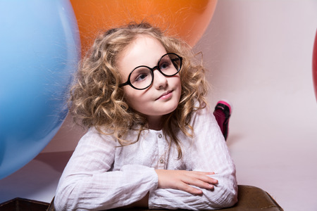 Portrait of curly teen girl in glasses on the background of large rubber balls. Girl looking to the sideの写真素材