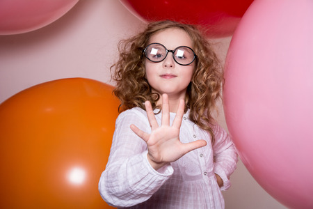 Portrait of a teenage schoolgirl showing five fingers on a background of large rubber balls. Happy girl looking at the cameraの写真素材