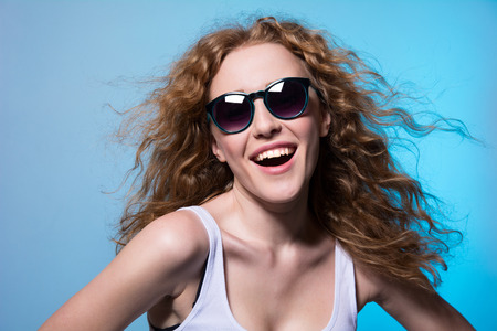 Pretty young emotional girl in sunglasses on a blue の写真素材