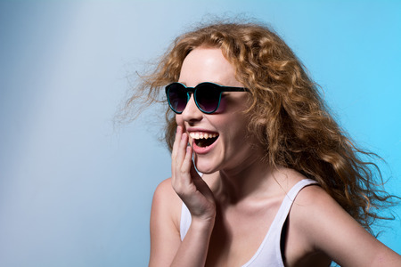 Pretty young emotional girl in sunglasses looking to the side on a blue の写真素材