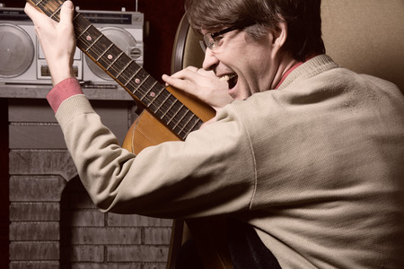 Adult cheerful man with acoustic guitar. Against the cassette player stands on the fireplaceの写真素材