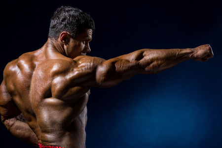 Handsome muscular bodybuilder posing over blue background. Trained athlete's bodyの写真素材