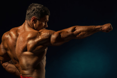Strong muscular man with outstretched hand to the side. Bodybuilder on a dark backgroundの写真素材
