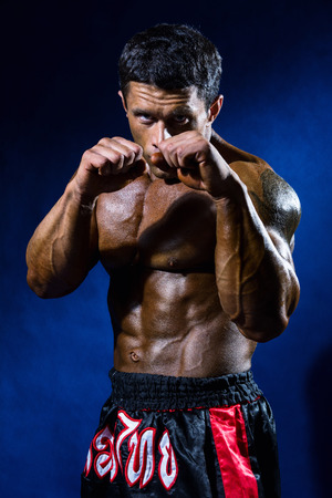 Fighter in a rack with fists on a blue background. Portrait of a kick-boxerの写真素材