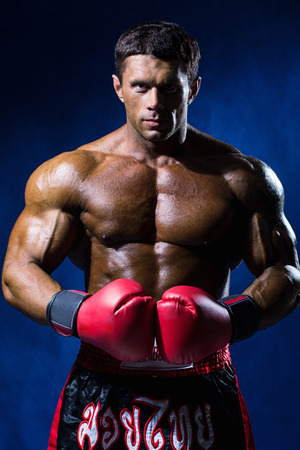Strong muscular boxer in red boxing gloves on a blue background.の写真素材
