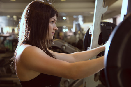Closeup of a young girl in the gym with a barbell. Woman trains his muscles on the simulator. Fitness, CrossFitの写真素材